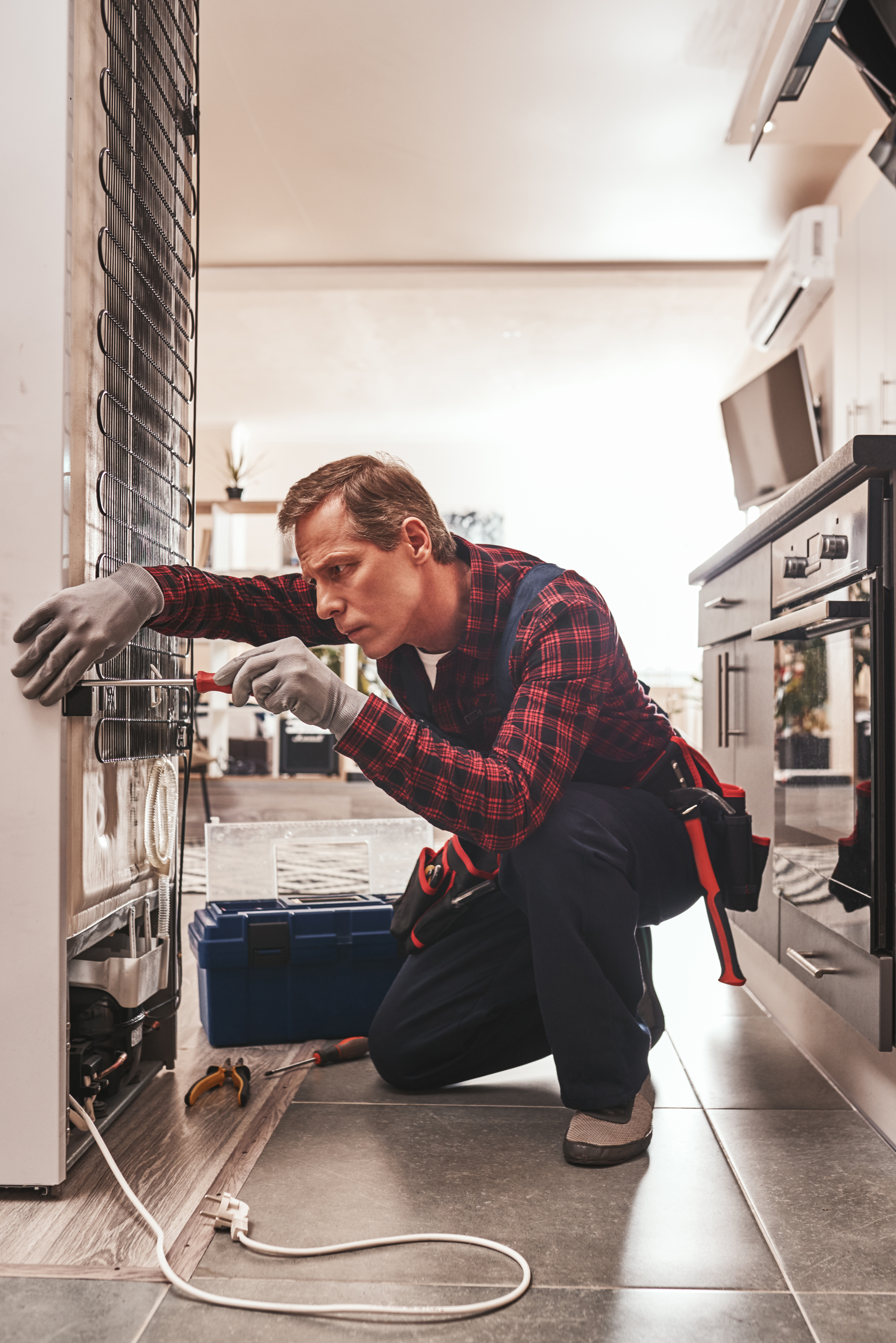 Should be attantive. Senior male technician checking refrigerator with screwdriver. He standing at knees. Side view